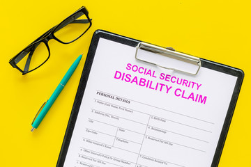 Social security. Disability claim form near pen and glasses on yellow background top view