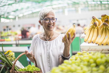 Good-looking senior woman buys bananas at the market