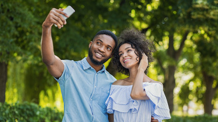 Cheerful lovely couple making selfie on smartphone outdoors