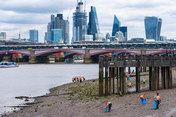 Volunteers cleaning the shores of the Thames from waste during low tide, Southbank, London
