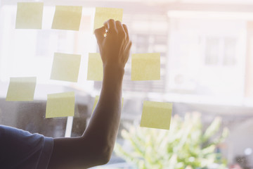 Hand holding pen and writing on sticky note papers which are on mirror wall. Business man writing on adhesive notes in creative office.selective focus