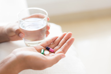 Closeup woman hand with pills medicine tablets and glass of water for headache treatment. Healthcare, medical supplements concept.