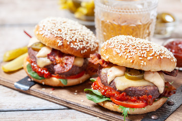 Two cheeseburgers on sesame buns with jalapeno on a rustic wood table
