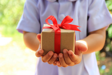 Selective focus of Little girl hands holding gift box with red ribbon for Christmas and New Year's Day or Greeting season