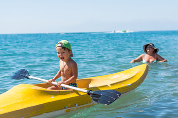 Grandmother and grandson smiling little baby boy  in green baseball cap kayaking at tropical ocean sea in the day time. Positive human emotions, feelings, joy.