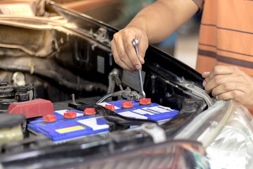 A man are removing the battery terminals from the car to work on the car electrical system using a wrench.