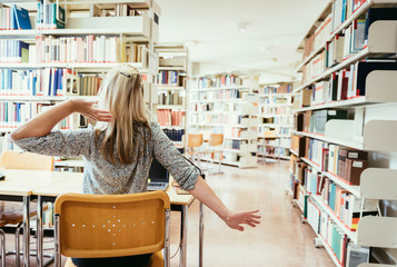 Junge blonde Frau streckt sich in der Bibliothek und lernt für Examen