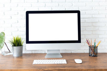 workspace with computer with blank white screen, and office supplies on a wooden desk