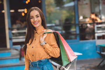 portrait of smiling stylish female shopper with shopping bags at city street