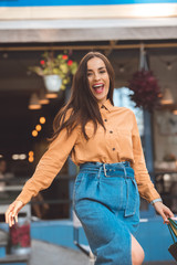 laughing young stylish female shopper walking with shopping bags at city street