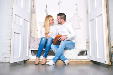 Fototapeta premium A beautiful happy young couple sitting in a wardrobe with christmas decorations and giving presents to each other.