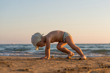 Smiling little baby boy running with splash in the sea on the beach at sunset.