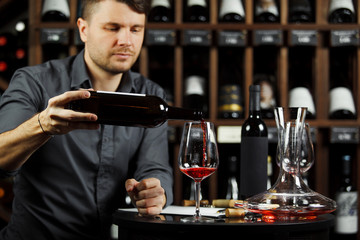 Sommelier pouring red wine from bottle in glass