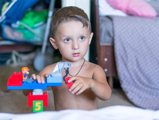 Little blond kid boy playing with lots of colorful plastic blocks indoor. Child having fun with building and creating.