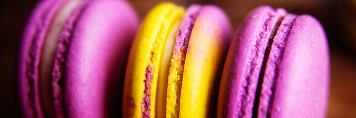 Colored macaroons pastel colors with different flavors on glass plate with paper towel. Bright and delicious dessert/ Wooden background