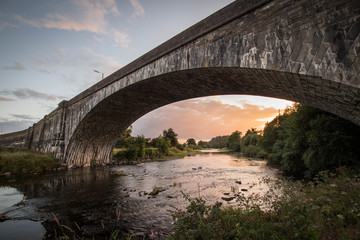 Fototapeta na wymiar Llandeilo single arch bridge with the river Tywi at sunset. pink and orange glow reflecting on the river.
