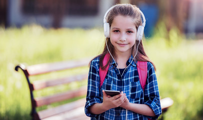 Happy schoolgirl enjoying in the park while listening to music with smartphone and headphones. Education, lifestyle, technology concept
