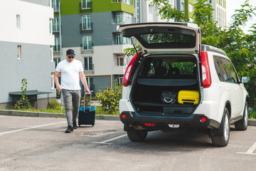 man pull suitcase with wheels to car trunk