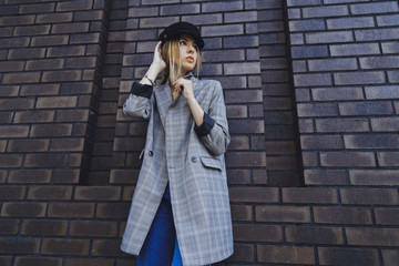 Young beautiful girl in a jacket, jeans and hat on a brick wall background
