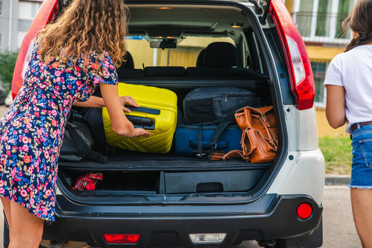 Two Woman Packing Luggage In Car Trunk