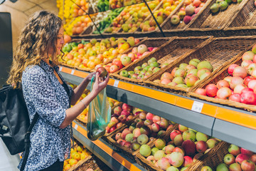 young adult woman choosing apples in grocery store