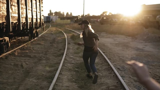 Backside footage of scared young woman running away from a zombie girl by railway. Sun shines on the background