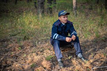 Policeman sits on the grass in the forest and thinks