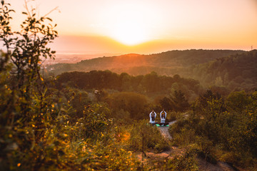 couple of women sitting at the edge of the hill. do yoga exercises on sunrise