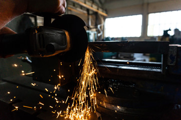 The worker polishes the metal with a grinding machine and sparks close-up.
