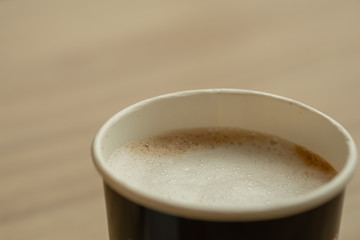 Close up of take away paper cup of hot coffee latte with milk foam