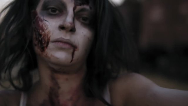 Portrait of a creepy female zombie with wounded face coming on . Blurred railway wagons on the background