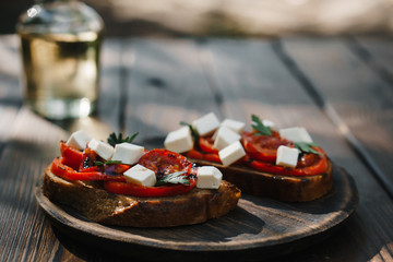 Tasty crunchy italian snack bruschetta with grilled tomatoes and feta cheese and bottle of olive oil on wooden table, delicious countryside organic snack