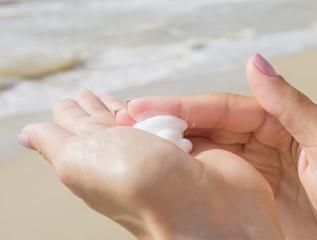 Woman using a bottle of sunscreen or sunblock cream on the tropical sundy beach. Close-up, part of body.