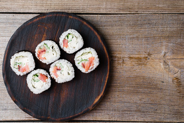 Japanese cuisine, food background. Tasty appetizing sushi rolls with salmon served on wooden plate, flat lay with copy space