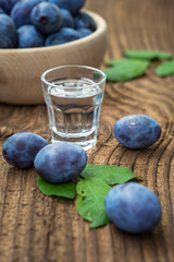 Fresh blue plums and plum brandy on wood table background. Sweet autumn fruit. Delicious and healthy raw food full of vitamins. Alcohol drink in glass dram.