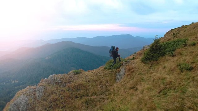 The man with a camping backpack climbing to the mountain on a sunset background