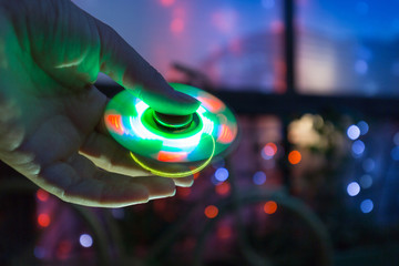 Girl playing with a Tri Fidget Hand Spinner outdoors on background of a night city. LED Glowing Hand toy.