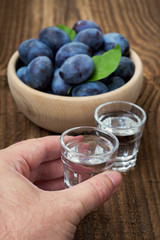 Fresh blue plums and plum brandy on wood table background. Sweet autumn fruit. Delicious and healthy raw food full of vitamins. Alcohol drink in glass dram.