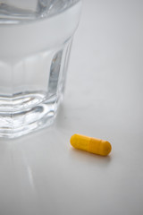 Gelbe Pillen Kapsel Medikament mit Glas Wasser