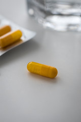 Zwei Pillenblister mit gelben Kapseln und Tabletten und Wasser Glas