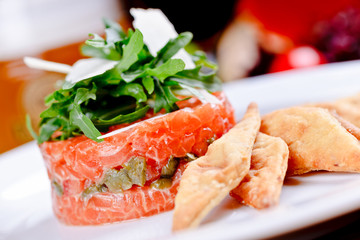 Salmon tartare with capers, arugula salad and parmesan cheese on white plate.