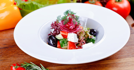 Greek salad with fresh vegetables, feta cheese and black olives on white plate. Close up.