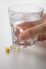 Frau nimmt zwei Gelbe Pillen Kapsel Medikament mit Glas Wasser