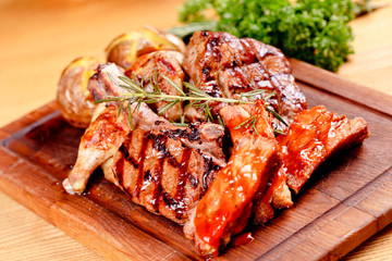Mixed grilled meat and potato on wooden cutting board. Pork, beef, poultry. Close up