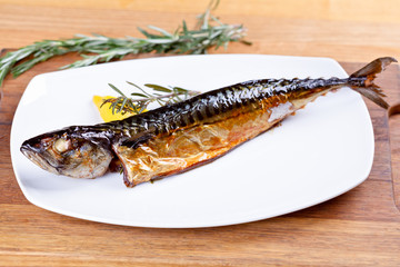 Smoked mackerel with rosemary and lemon slice on white plate. Close up