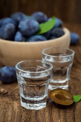 Fresh blue plums and plum brandy on wood table background. Sweet autumn fruit. Delicious and healthy raw food full of vitamins. Alcohol drink in glass dram.