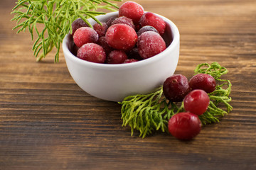 Cranberries in a white bowl on a wooden board. Frozen cranberries. Cranberry with moss in a white bowl.