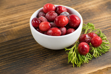 Cranberries in a white bowl on a wooden board. Frozen cranberries. Cranberry with moss in a white bowl.