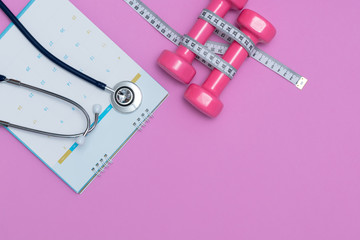 Stethoscope and a calendar. Doctor's appointment and service in the hospital. Dumbbell and measure tape on pink background. Medical starvation. Diet for weight loss concept. 