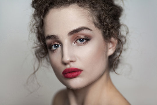 closeup beauty portrait of young beautiful fashion model with collected dark curly hair, nude makeup and red lips looking at camera with serious face. indoor studio shot. isolated on gray background.